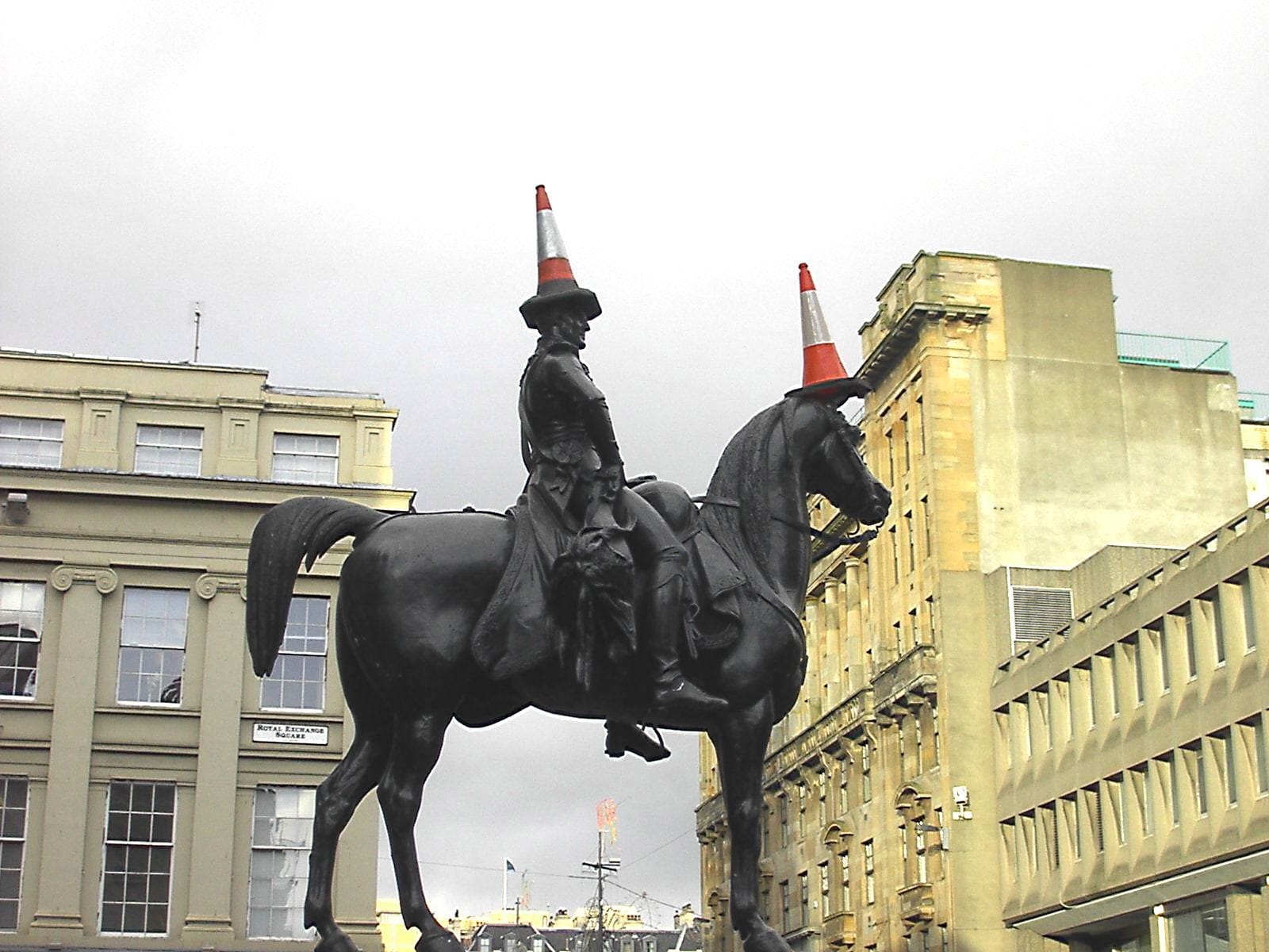 A Glashow statue of a man on a horse. Both have a traffic cone on their heads. 