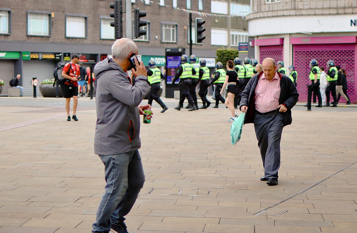 a street scene with a group of police officers in high-visibility vests walking in formation in the background.