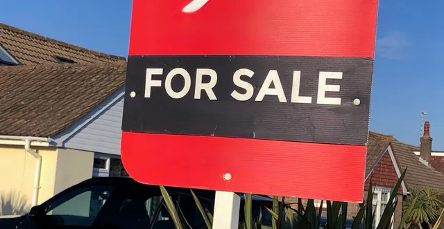 A red for sale board in front of a suburban house. 